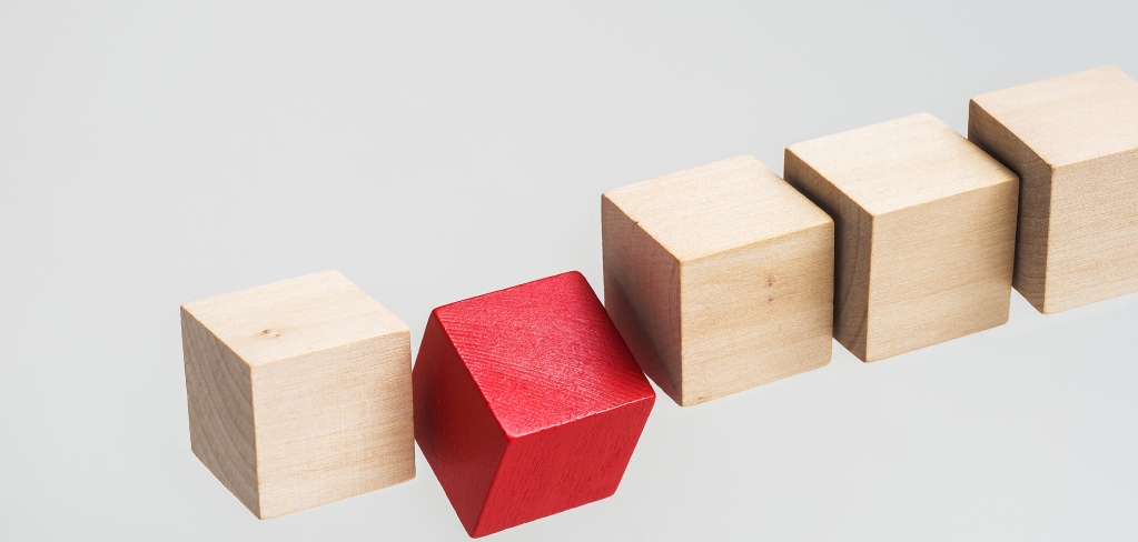 A red block falls out of line among plain wooden blocks, representing customization.