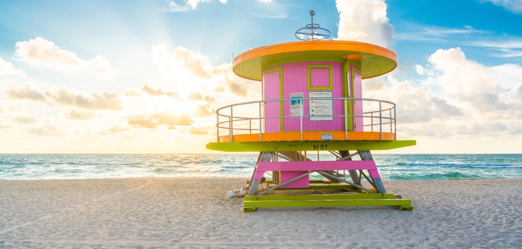 A pink, orange, and yellow lifeguard station pagoda on a sunny beach.