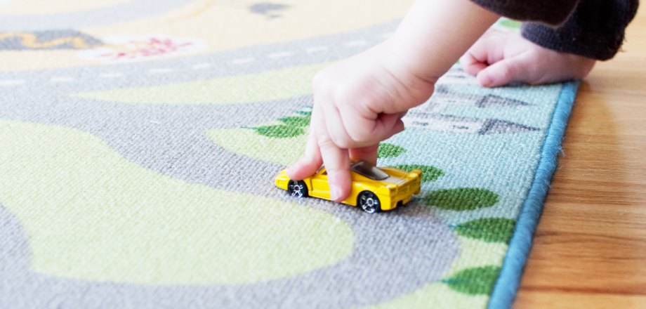 Child playing with toy car on a rug map