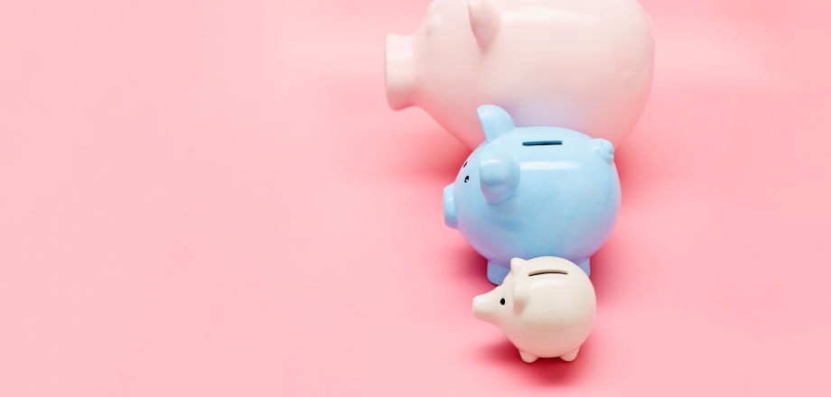 two light pink piggy banks and one light blue piggy bank in a row, largest at the top and smallest at the bottom,  with a pastel pink background