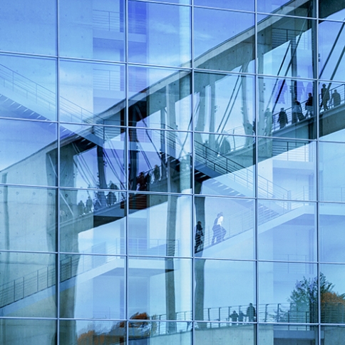 Blue glass office building with people walking around inside.